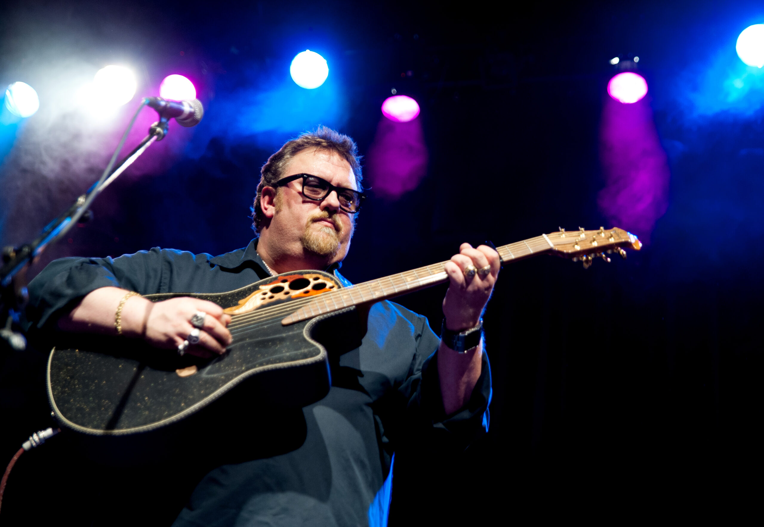J.P. Cormier playing a guitar on stage with blue and purple lighting